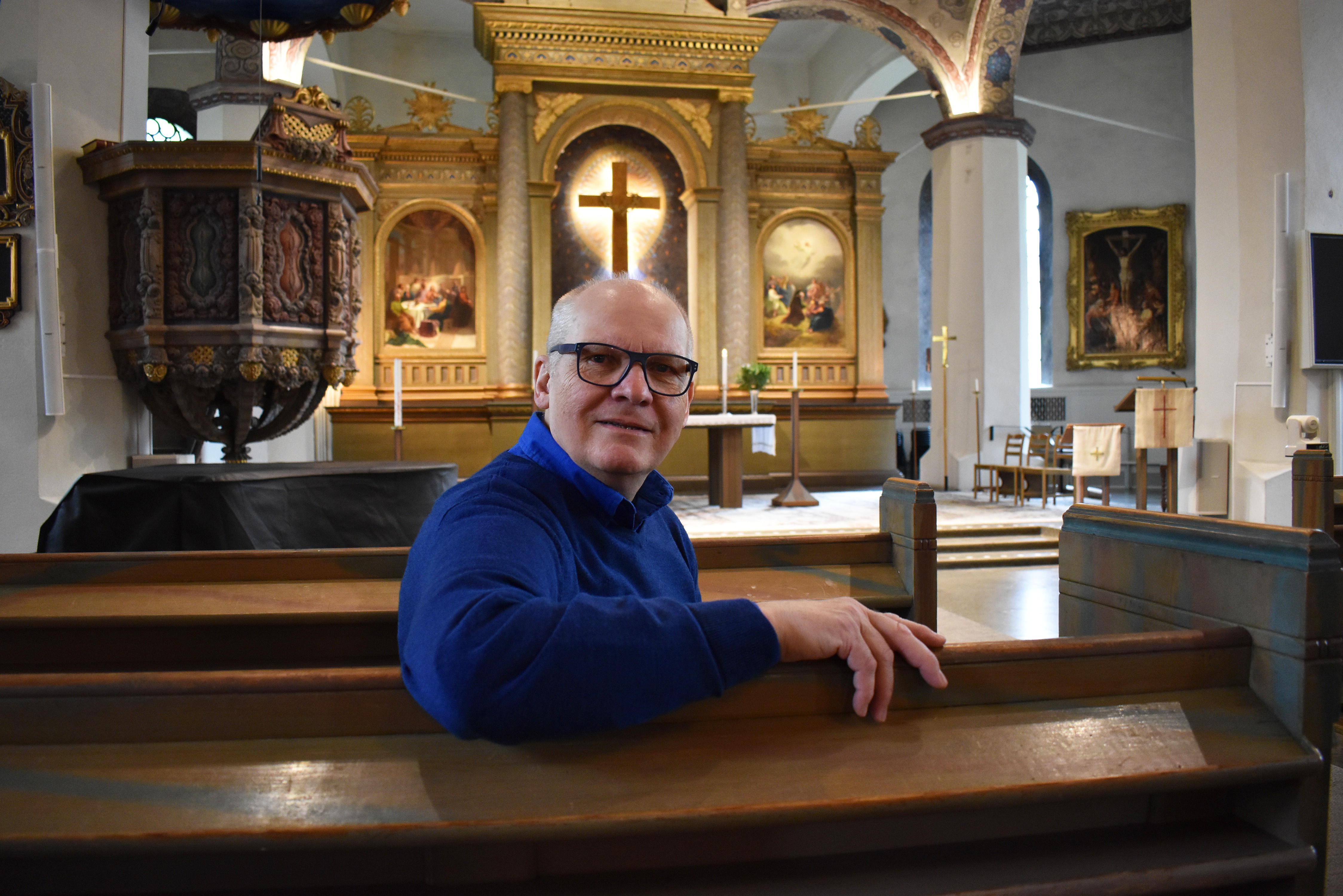 Christer Säll, ideell medarbetare i Caroli kyrka, sitter i kyrkbänkarna med altaret i bakgrunden.