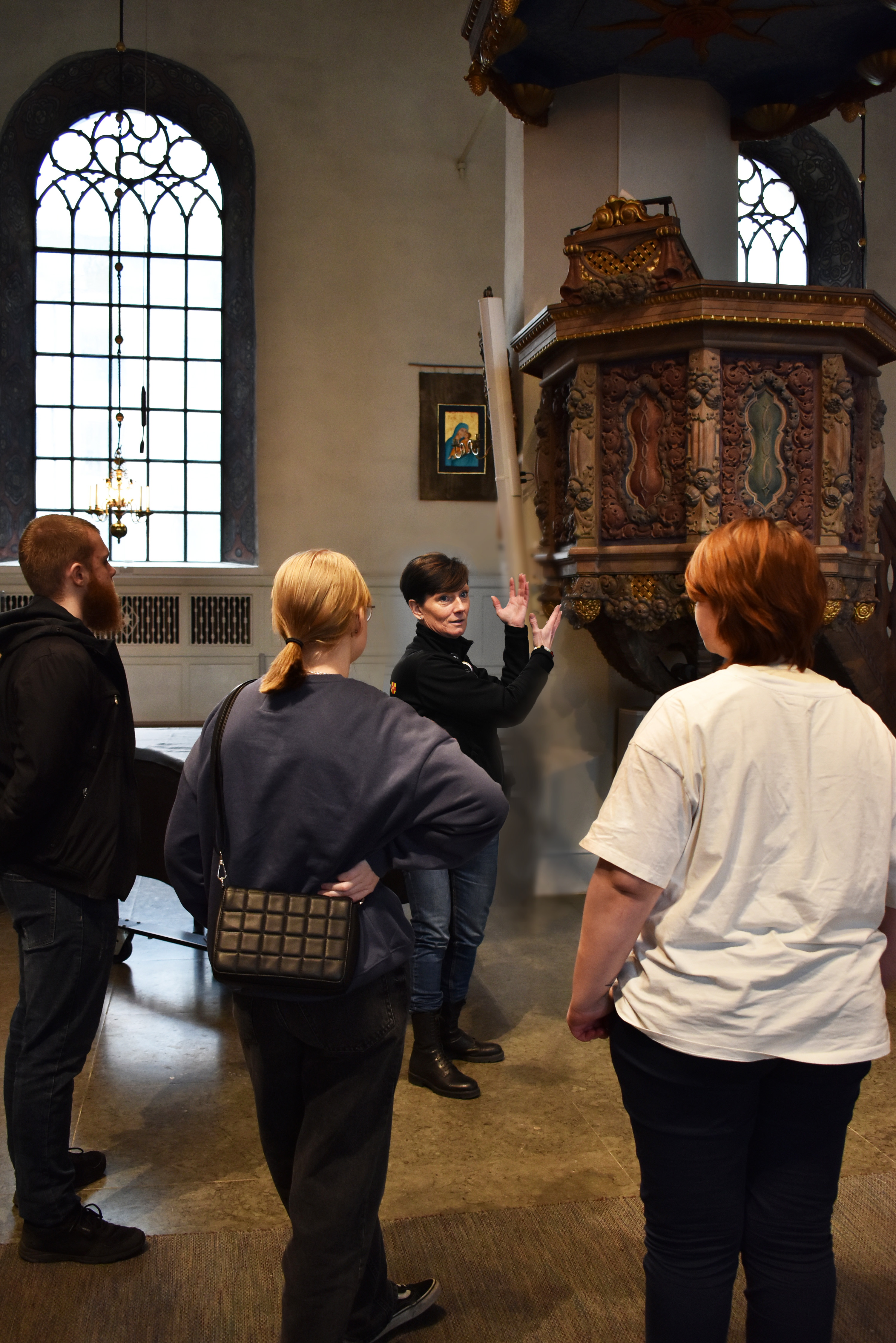 Kvinna gestikulerar inför ungdomar i en kyrka.