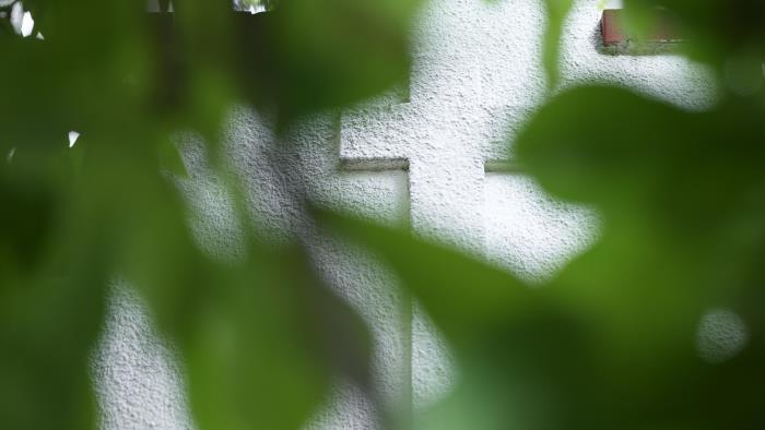 Bakom några gröna löv syns ett kors på en husfasad.