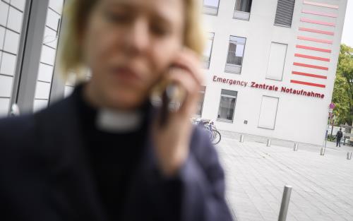 En kvinnlig präst pratar i telefon utanför ett sjukhus.