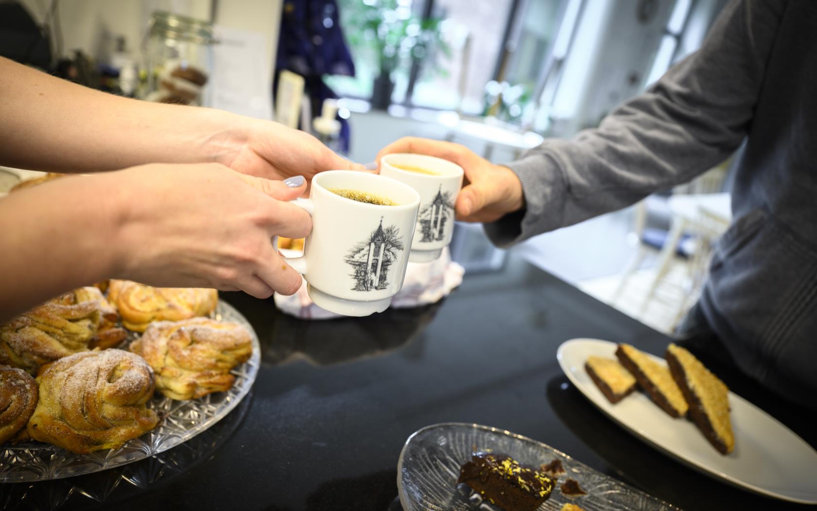 Någon räcker över en kopp kaffe över ett fikabord.