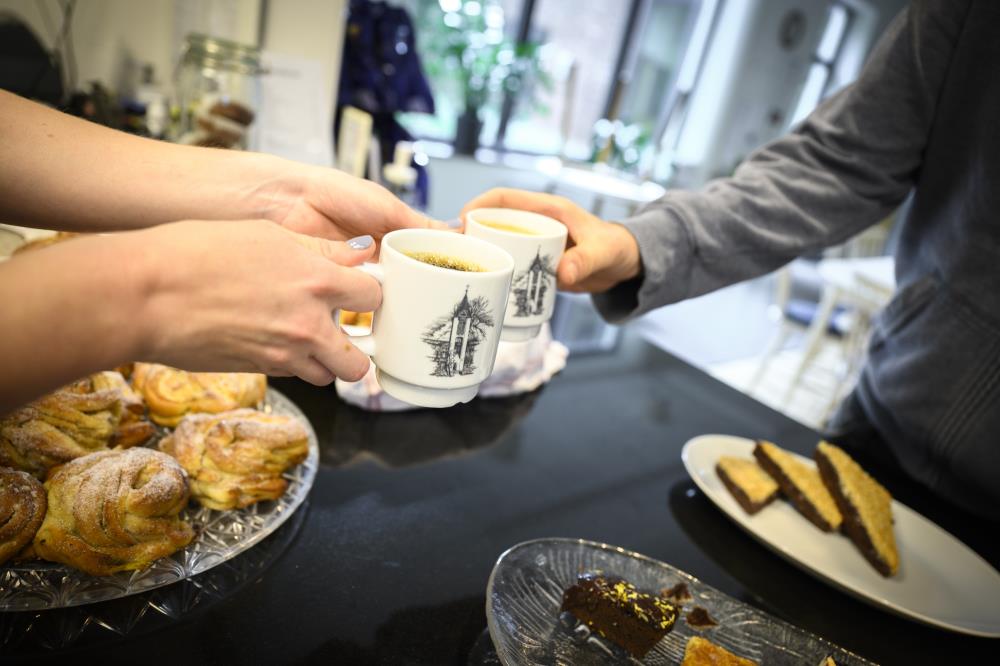 Någon räcker över en kopp kaffe över ett fikabord.