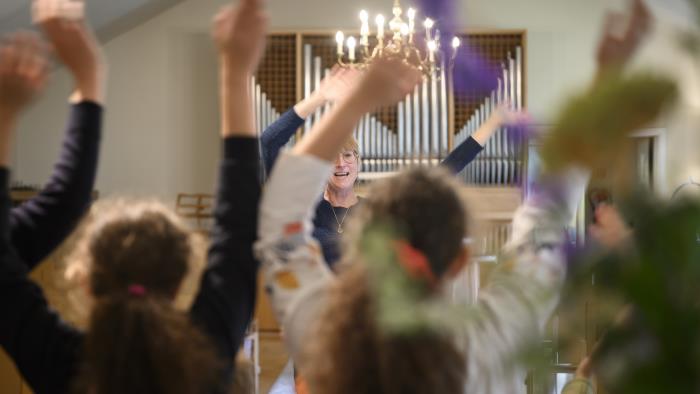 Några ungdomar står i en kyrka och viftar med armarna i luften. En kvinna står framför dem och gör likadant.