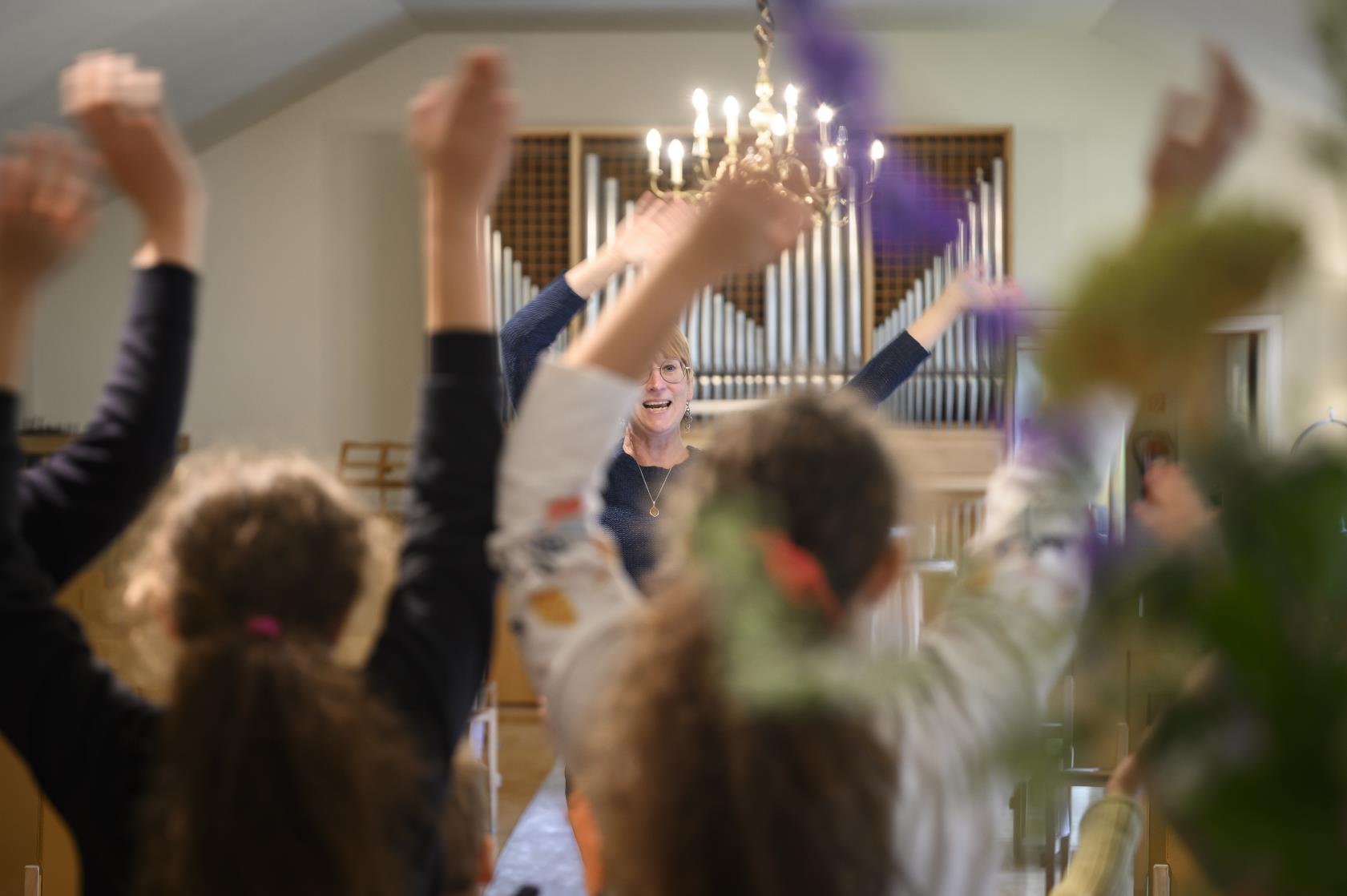 Några ungdomar står i en kyrka och viftar med armarna i luften. En kvinna står framför dem och gör likadant.