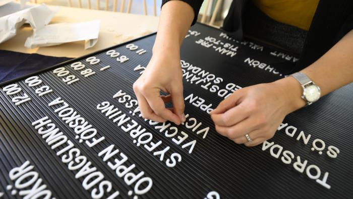En person trycker fast bokstäver till ett veckoschema på en tavla.