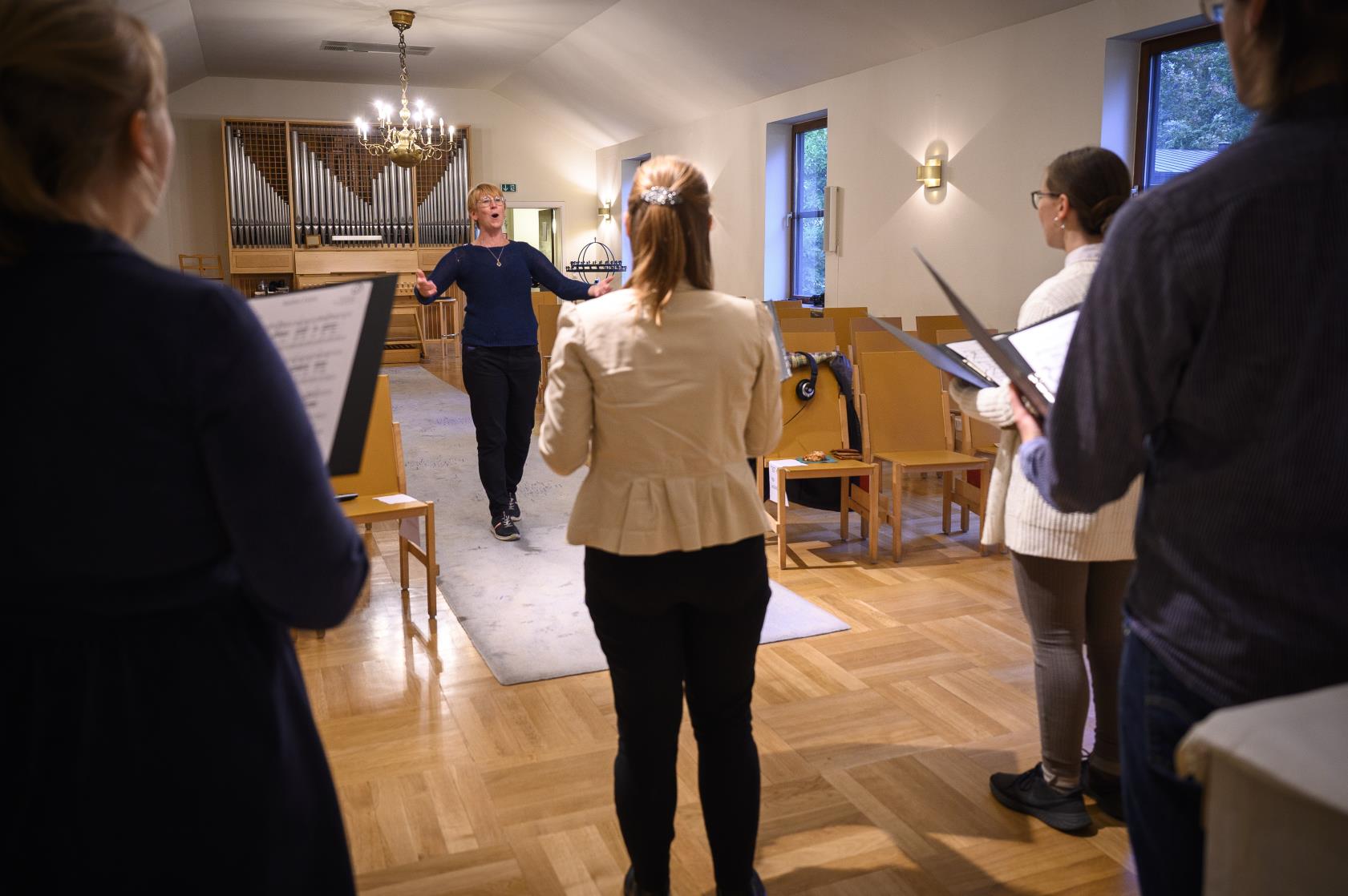 En kvinnlig körledare dirigerar sin kör i en kyrka.