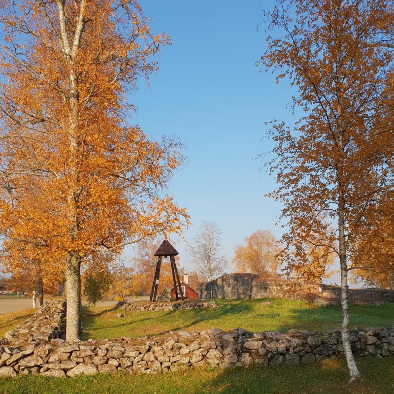 Kyrkoruin och klockstapel omgivna av träd i höstskrud