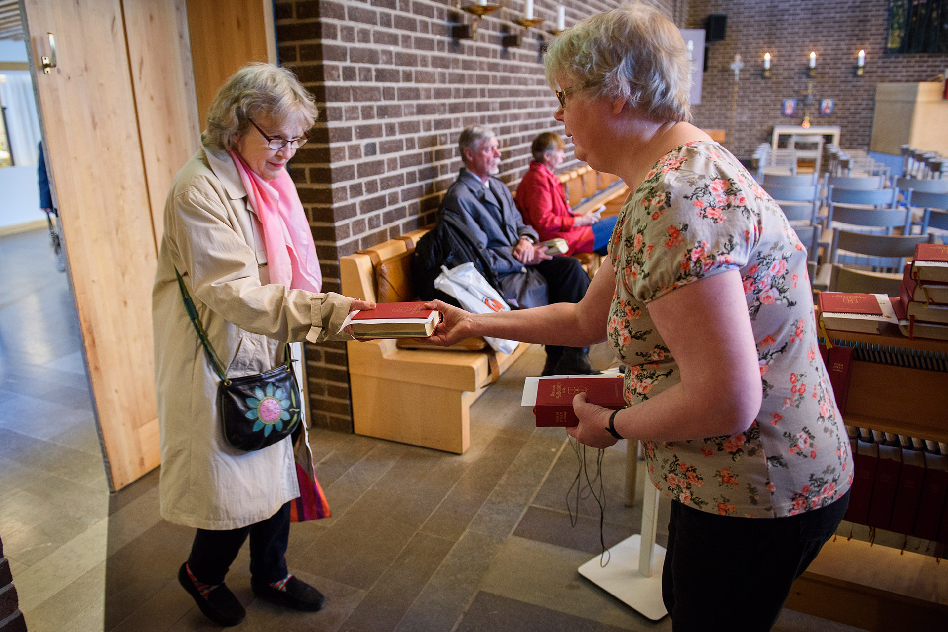 Kyrkvärd tar emot gudstjänstdeltagare i Skärholmens kyrka.