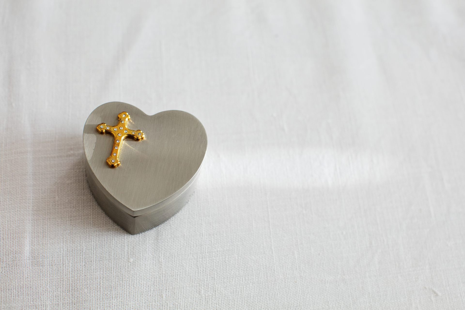 En silvrig ask format som ett hjärta och dekorerat med ett kors ovanpå.