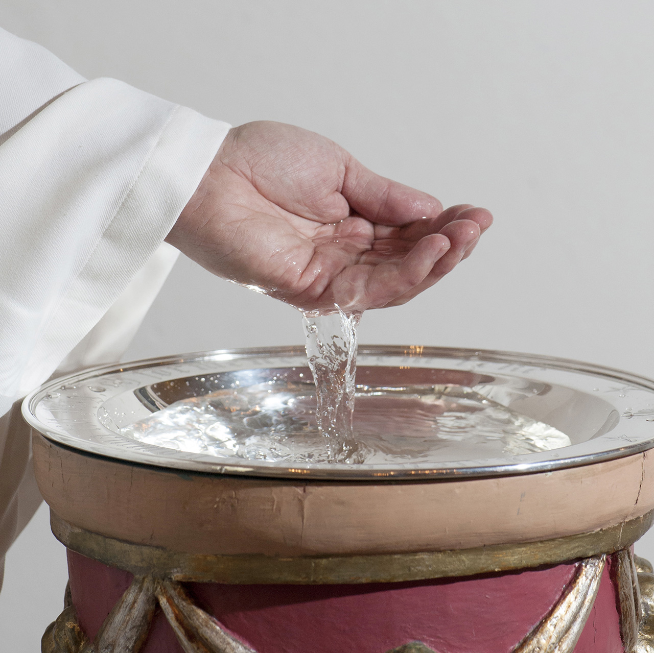 En person har vatten i sin hand och häller ner det i en dopfunt.