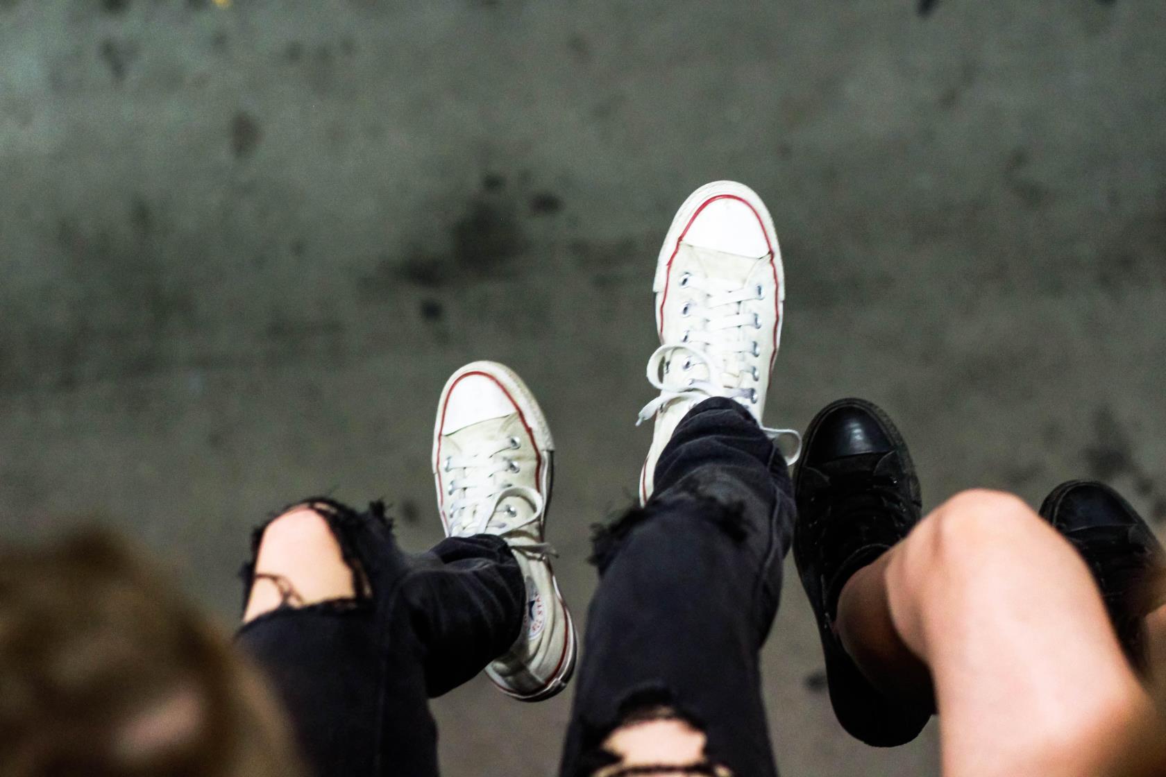 Sneakersbeklädda fötter och ben på ungdomar som sitter och dinglar med benen