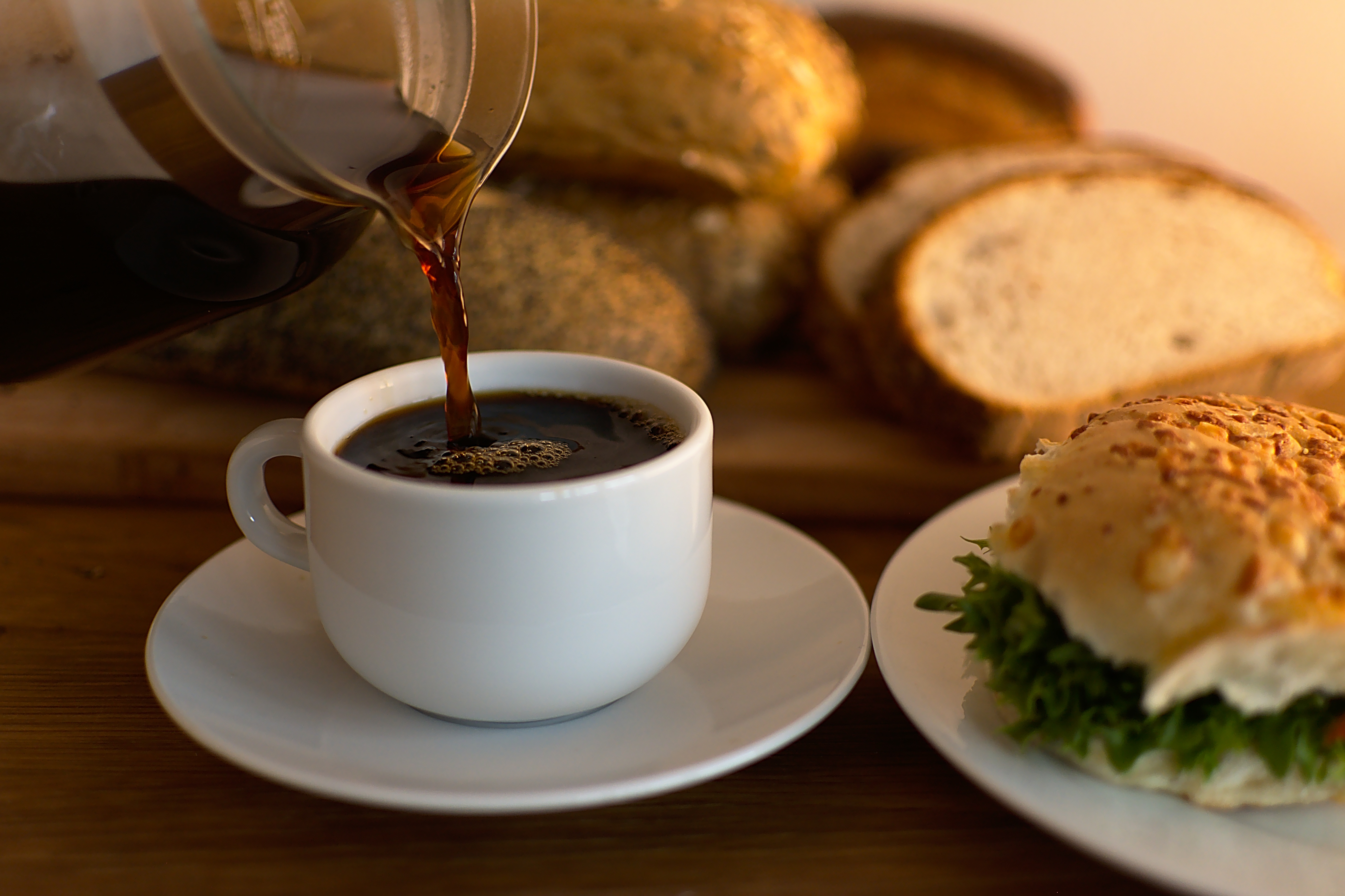 Person häller upp kaffe i en kopp och bredvid finns en bulle och bröd.