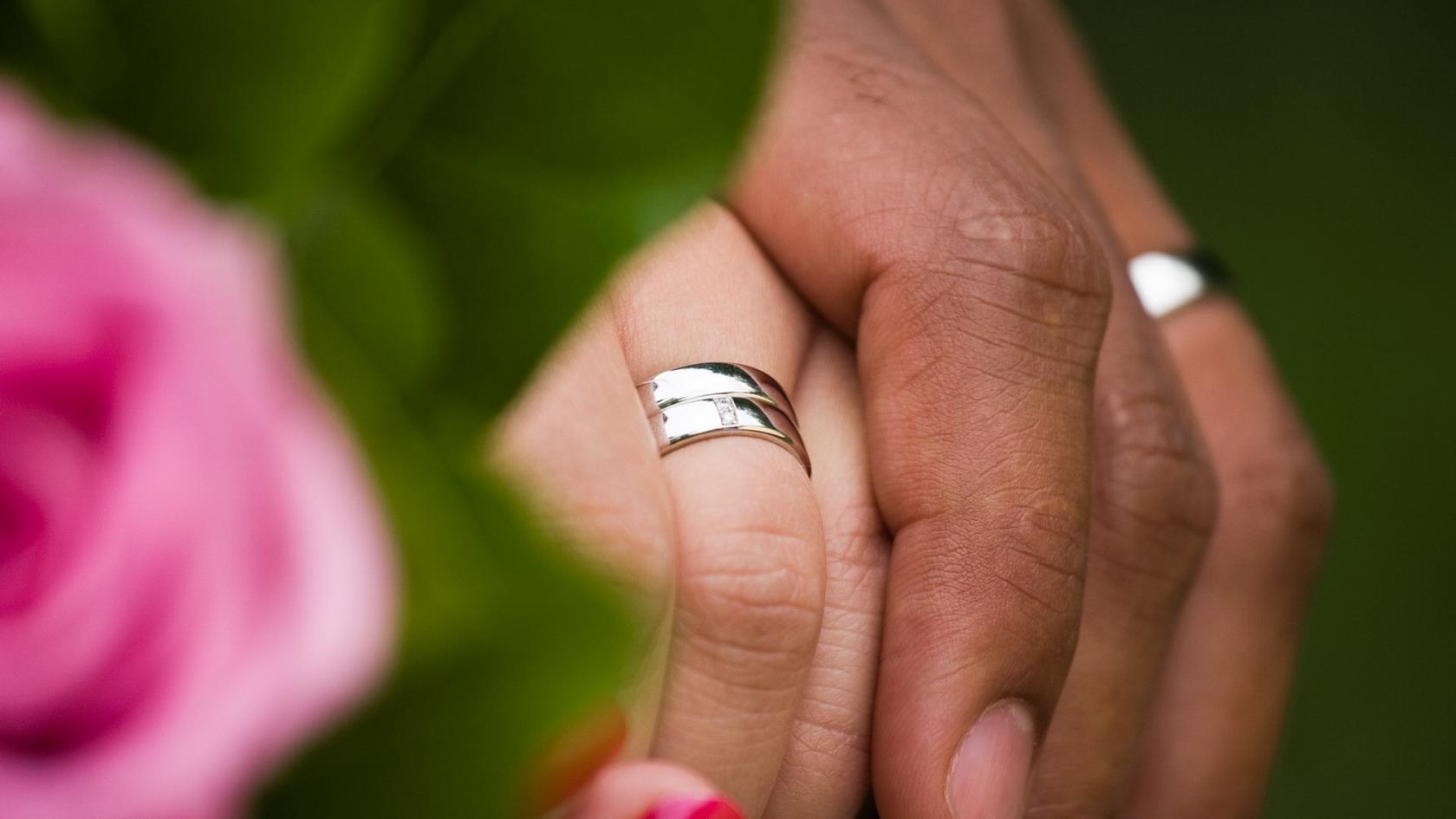 Vigselringar i silver på ett gift pars händer som håller hand.