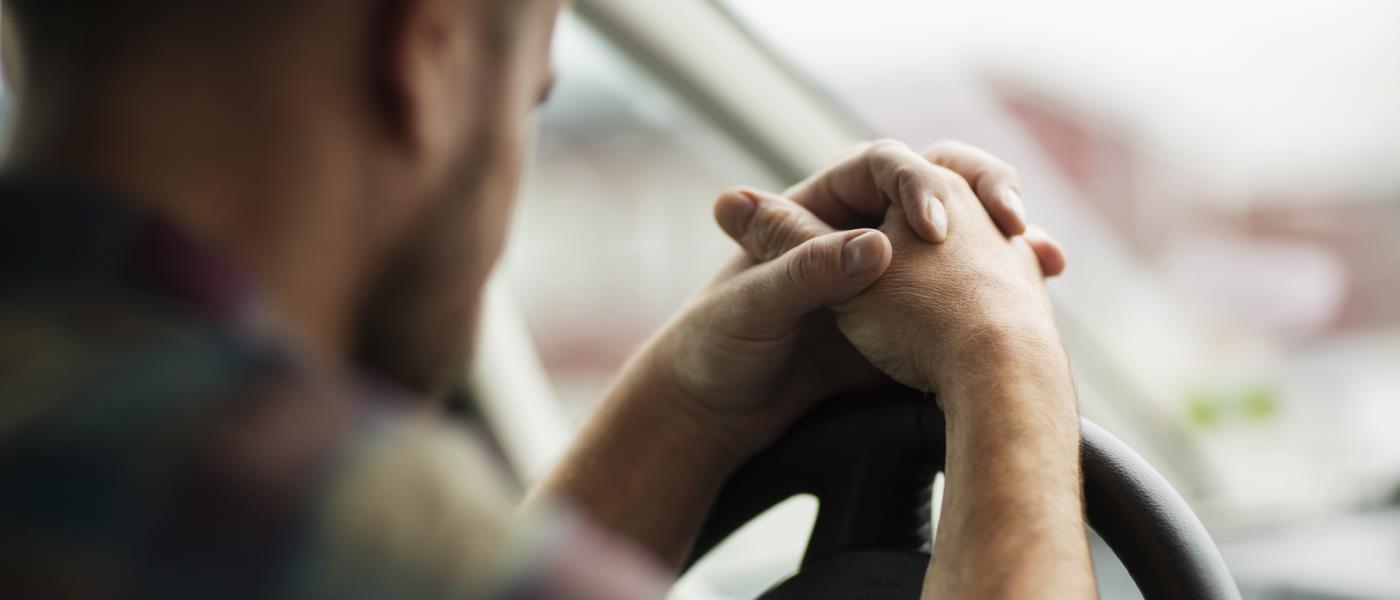 En man sitter i bilen med händerna knäppta på ratten.